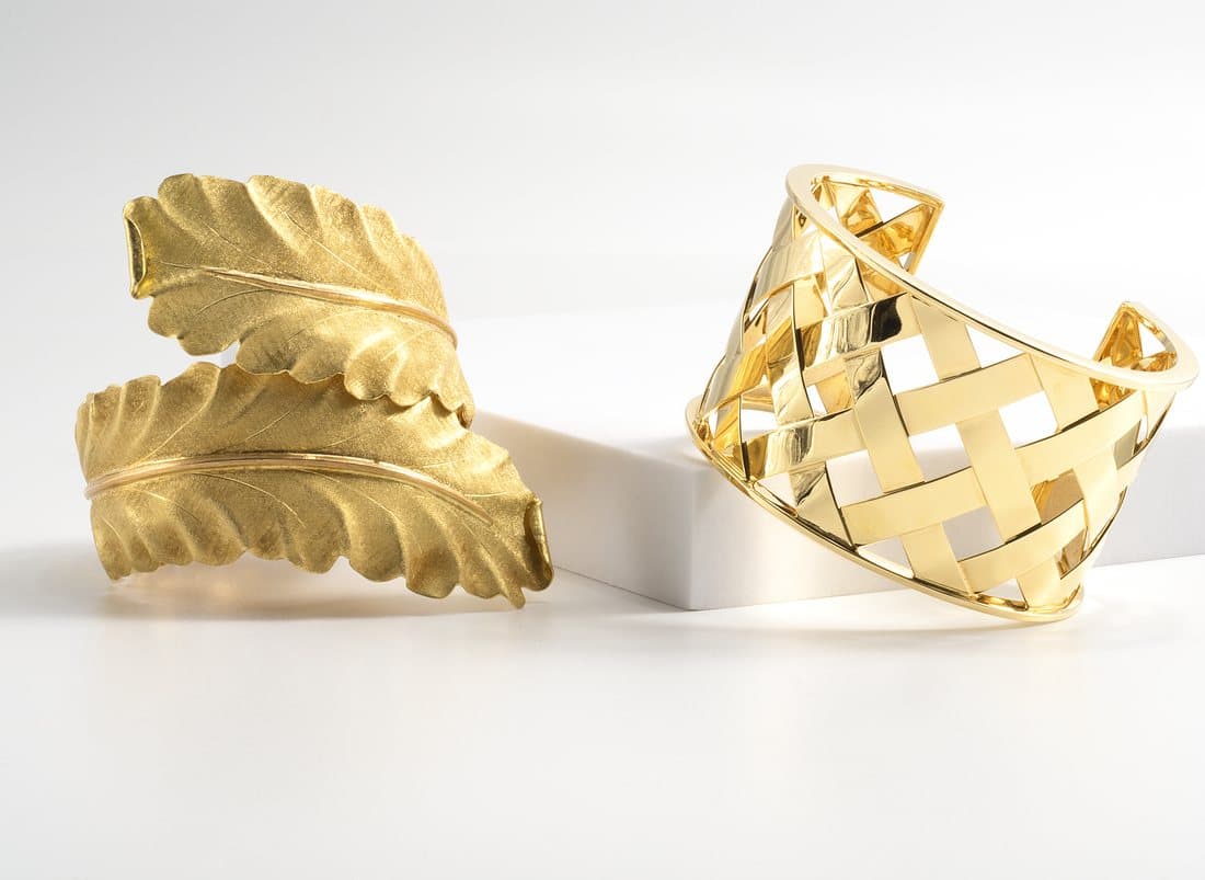 Two yellow-gold cuff bracelets on white studio blocks